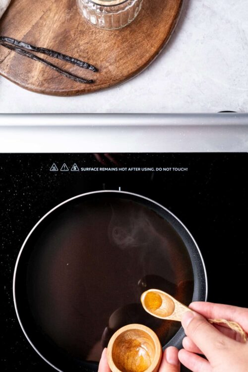 Vanilla extract being added to a black stovetop pot, cooking ingredients for baking.