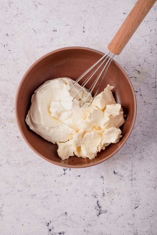 Cream cheese in a bowl with a whisk.