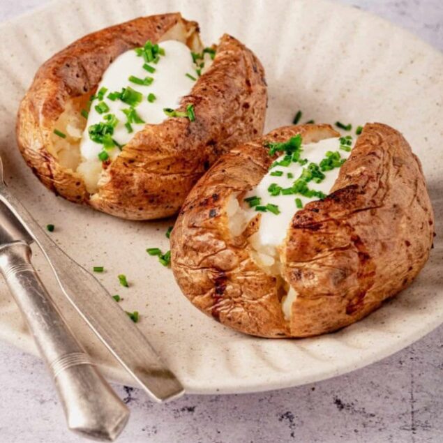 Baked potato with creamy butter and chopped chives on a beige plate.