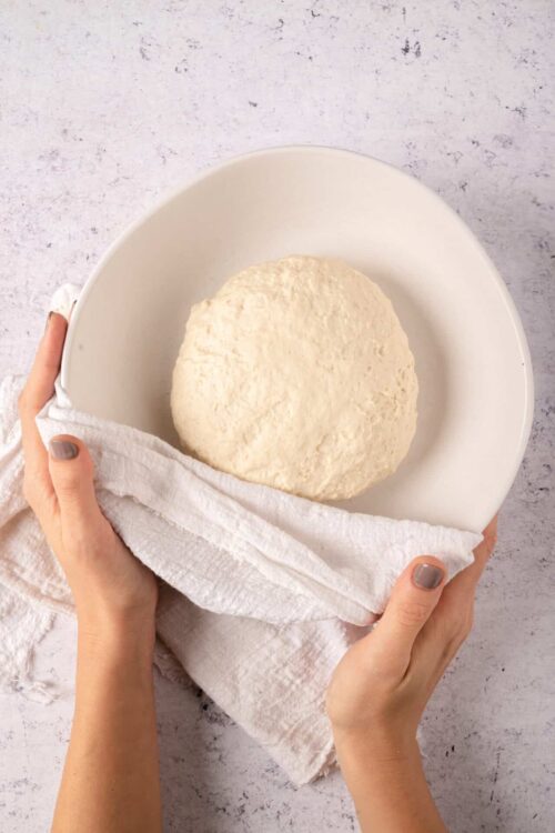 Freshly kneaded bread dough resting in a white bowl.