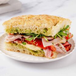 Soft broccoli and cheese focaccia sandwich with fresh vegetables on a white plate.