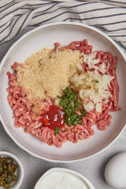 Freshly prepared ingredient mixture for homemade meatballs with breadcrumbs, onions, herbs, ketchup, and seasonings.