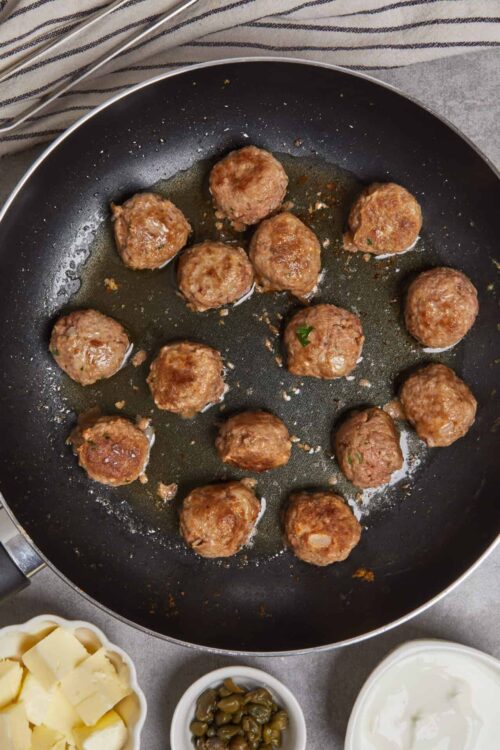 Juicy homemade meatballs cooking in a black skillet with herbs and seasoning.