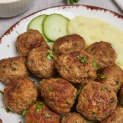 Savory meatballs with parsley served with cucumber slices and mashed potatoes on a decorative plate.