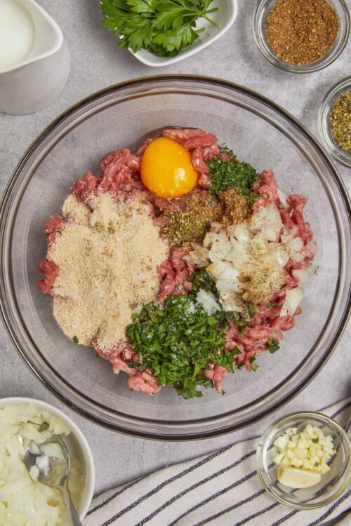 Minced beef mixture with egg and herbs for meatloaf preparation.