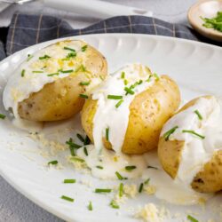 Baked potatoes with sour cream and chives on a white platter, ready to serve.
