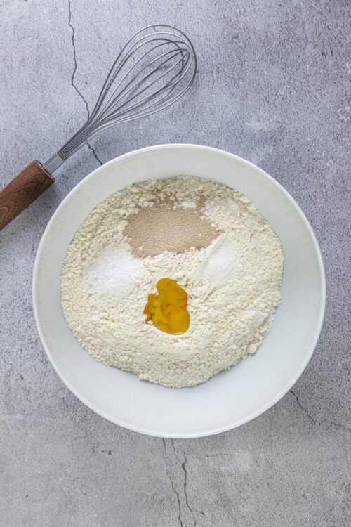 Flour mixture with egg, yeast, and seasonings in a white bowl for baking bread or pastries.