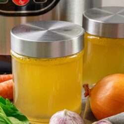 Golden homemade chicken broth in glass jars with fresh vegetables.