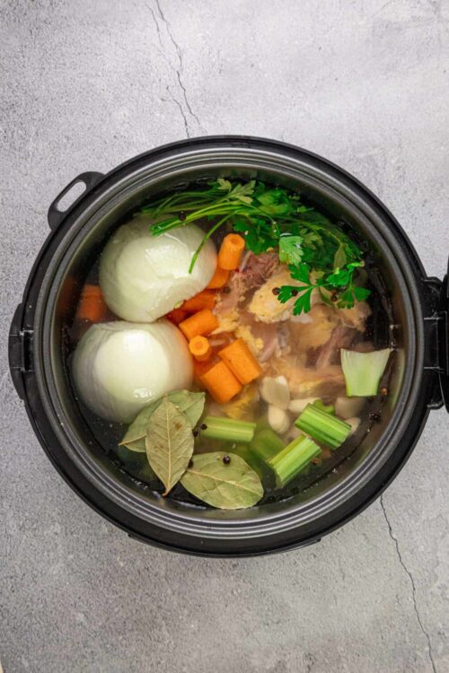 Rich homemade vegetable broth in a slow cooker with carrots, onions, garlic, celery, bay leaves, and fresh herbs.