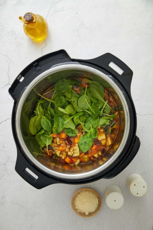 Fresh ingredients inside an Instant Pot, cooking a vegetable stew with spinach and diced vegetables.