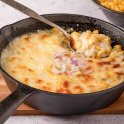 Creamy cheesy casserole with corn and onions in a cast iron skillet.
