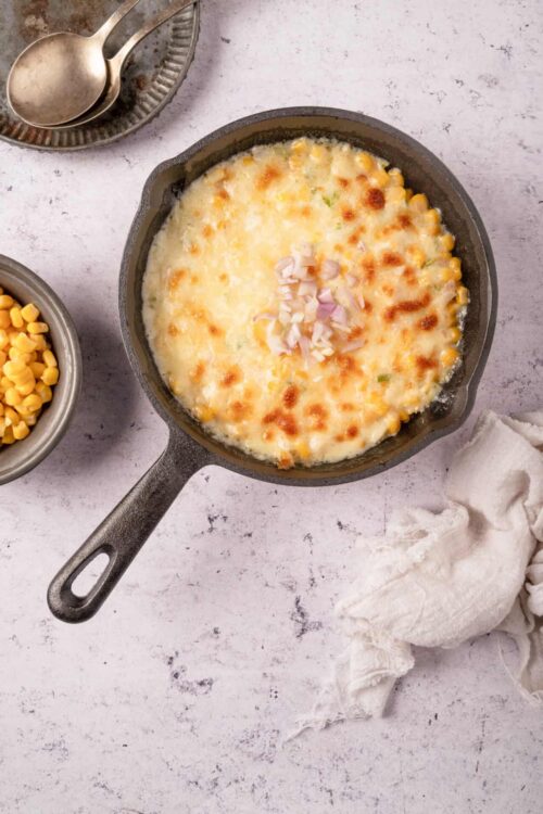 Creamy corn casserole baked in cast iron skillet with cheese and onions.