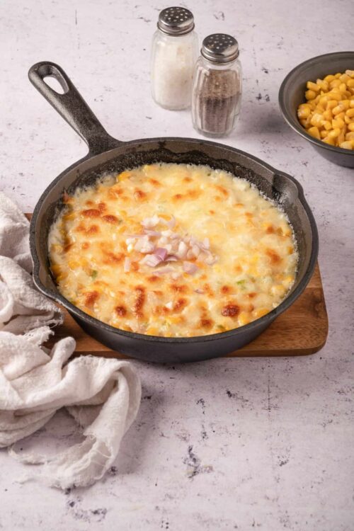 Creamy baked macaroni and cheese in a cast iron skillet topped with melted cheese and onions.