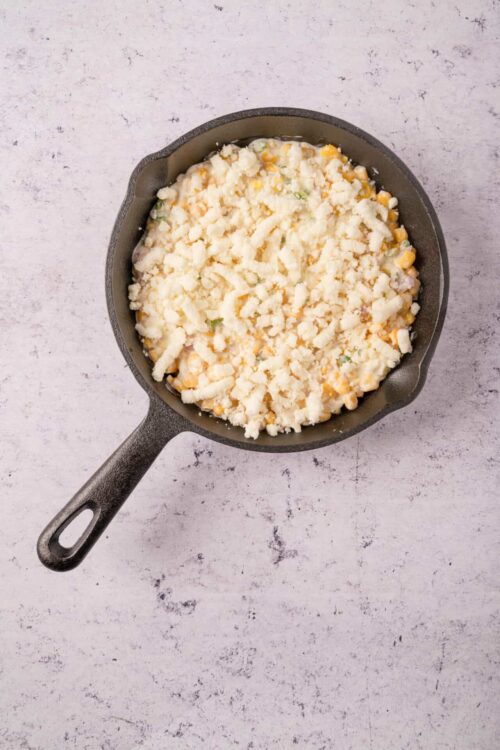 Creamy corn casserole in a skillet with shredded cheese and vegetables.