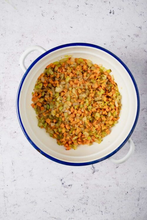 Diced celery, carrots, and onions in a white baking dish with blue rim, ready for cooking.