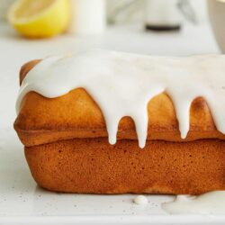 Fluffy lemon loaf cake with lemon glaze on a white cutting board. Perfect for lemon desserts and baking recipes.
