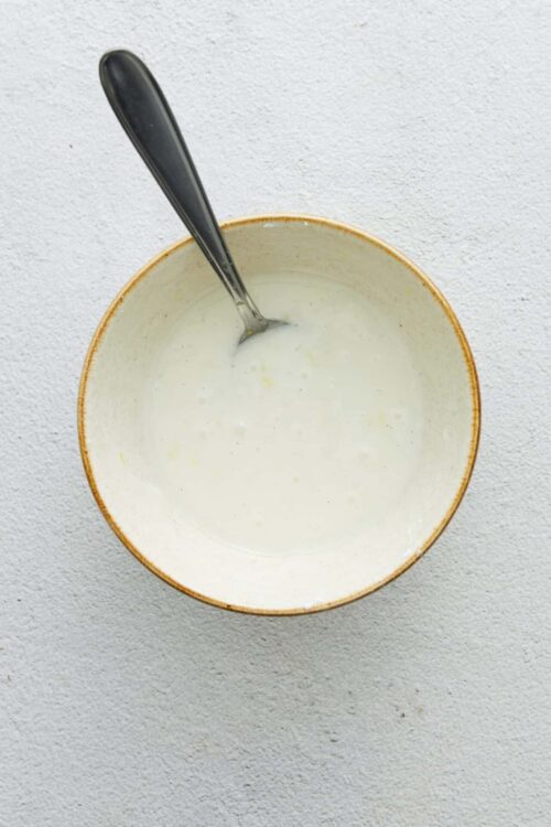 Creamy homemade ranch dressing in a rustic bowl with a spoon.