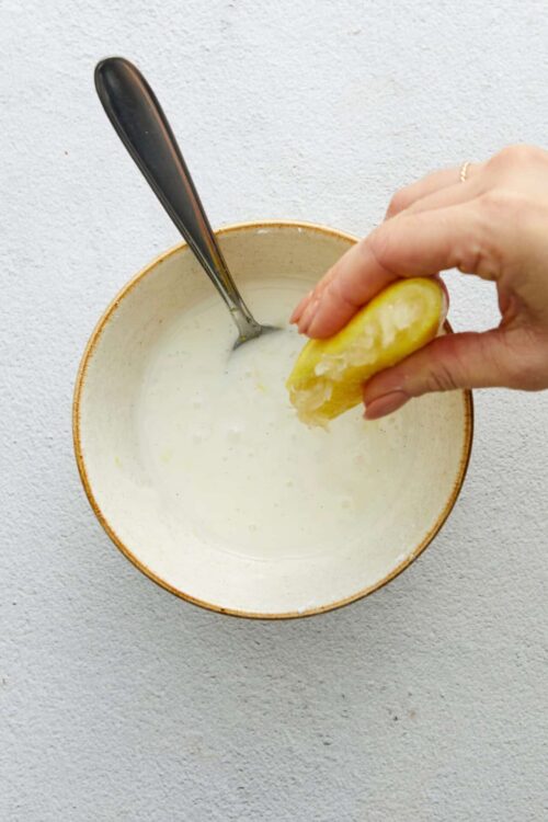 Freshly squeezed lemon being added to homemade yogurt in a ceramic bowl.