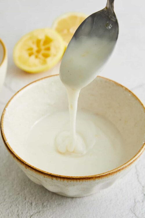 Lemon curd being stirred in a rustic bowl with fresh lemons in the background.