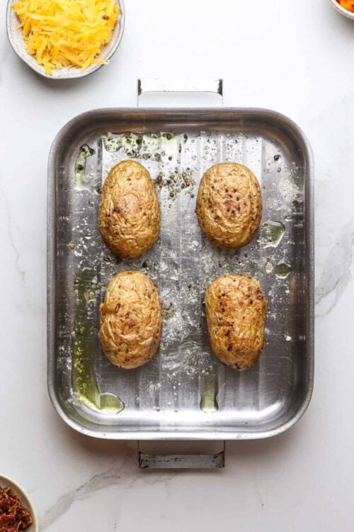 Baked sweet potatoes on a metal baking sheet with olive oil remnants and seasoning.