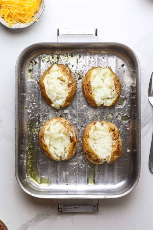 Baked potatoes stuffed with creamy mashed potatoes, on a metal baking sheet.