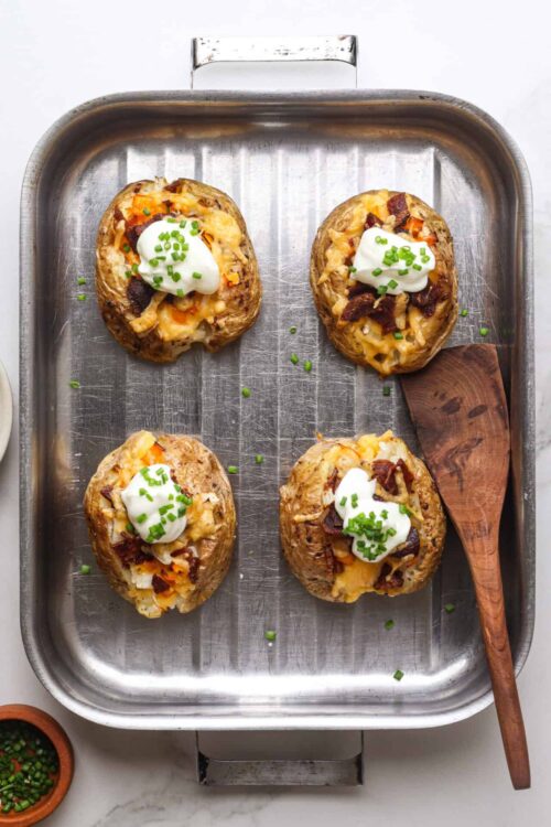 Baked stuffed baked potatoes topped with cheese, sour cream, and chives.