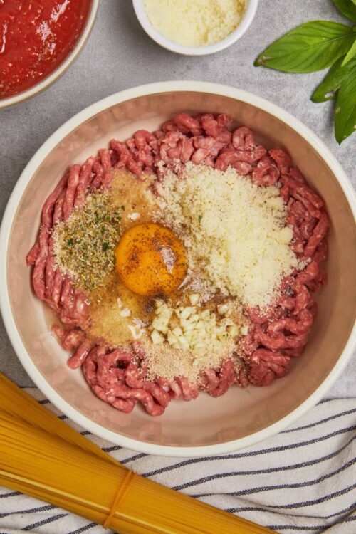 Ground beef mixture with egg, garlic, and seasoning for meatball recipe.
