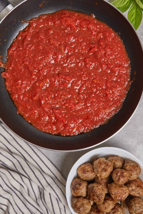 Savory homemade spaghetti sauce simmering in a skillet with cooked meatballs in a bowl.