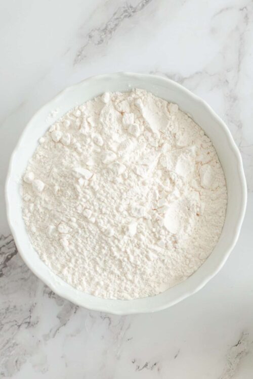 Powdered flour in a white bowl on marble surface.