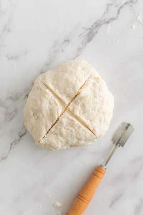 Freshly made pie dough ball on marble surface with pastry cutter.