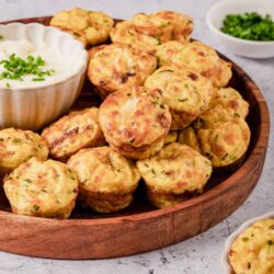 Golden baked crab cakes with chives served with creamy dipping sauce on a wooden platter.