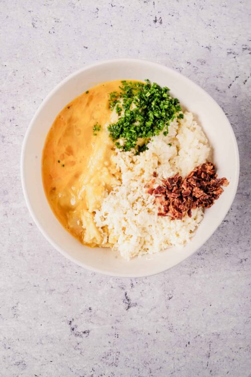 Creamy mashed potatoes with chopped chives, crumbled cheese, and bacon bits in a white bowl.