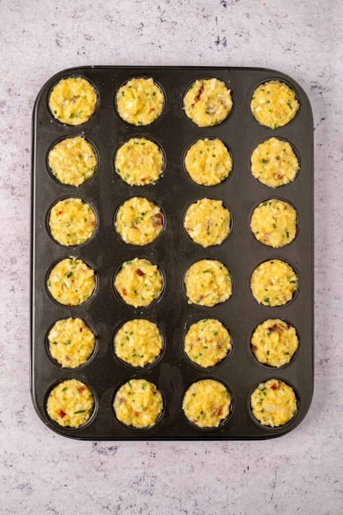 Cream cheese and chive breakfast muffins in a black muffin tin, ready to bake.