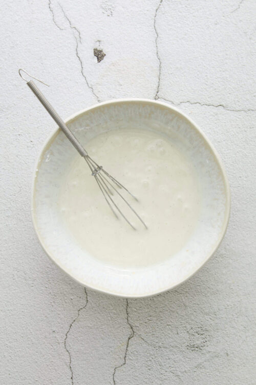 Fluffy white batter in a mixing bowl with a whisk on a textured surface.