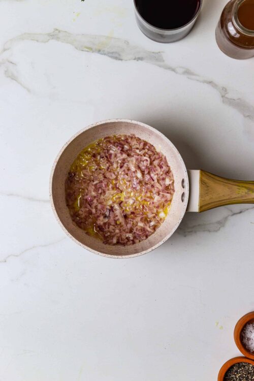 Sauteing diced onions and garlic in a pink non-stick skillet on a white marble countertop for cooking.