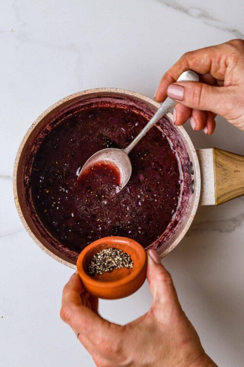 Sweet berry syrup being stirred in a saucepan with a small spicy chili pepper on the side, ready to be used for baking or dessert topping.