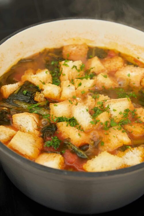 Savory vegetable and bread soup with herbs in a cooking pot.