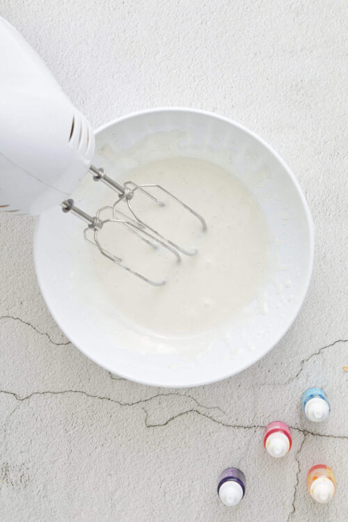 Fluffy whipped cream in a white bowl with electric hand mixer.