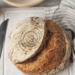 Rustic sourdough bread with a cracked crust on white cutting board.