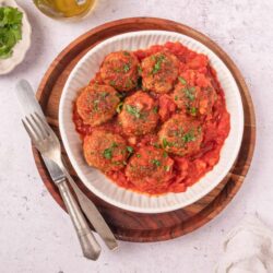 Savory Italian meatballs in tomato sauce on white dish with herbs.