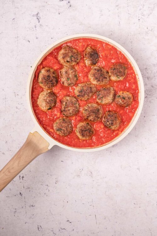 Savory meatball skillet in tomato sauce on a white baking dish.
