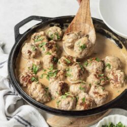 Creamy Swedish Meatballs in sauce garnished with parsley in a black skillet.