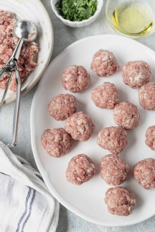 Raw meatballs made with ground beef on a white plate for baking. Perfect for homemade meatball recipes and Italian cuisine.