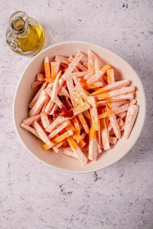 Fried sweet potato fries in a white bowl with seasoning and olive oil.
