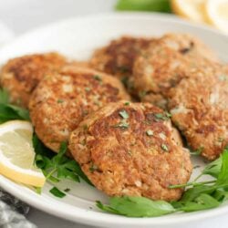 Crispy crab cakes with lemon wedges on white plate.
