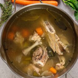 Savory chicken vegetable broth with carrots and herbs in a pot.
