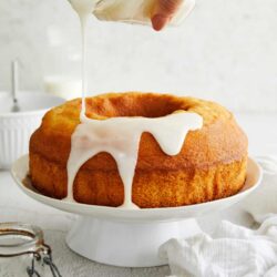Cream pouring over a golden bundt cake on a white cake stand.