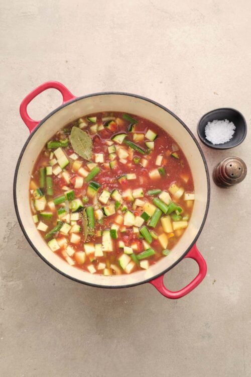 Chopped zucchini, tomatoes, and herbs simmering in a soup pot with spices.