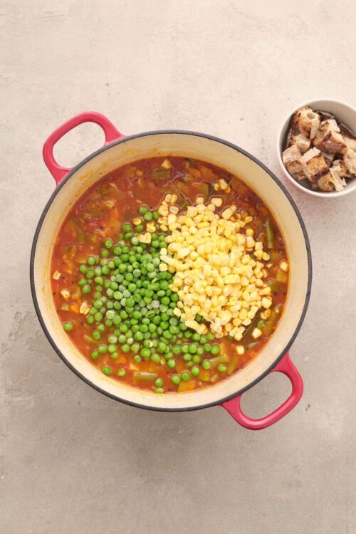 Vegan vegetable soup with peas and corn in a red enameled cast iron pot.