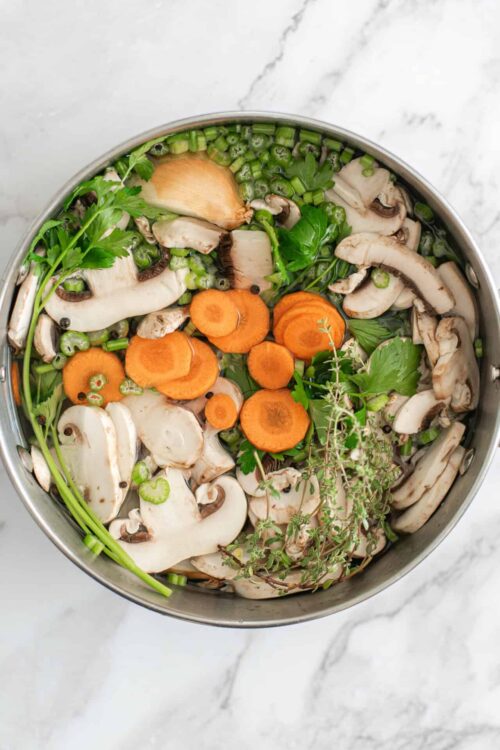 Fresh vegetable soup ingredients in a pot on a white marble surface.